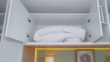 Een net opgemaakt bed in een witte kamer, met een houten hoofdeinde en een nachtkastje met een lamp.