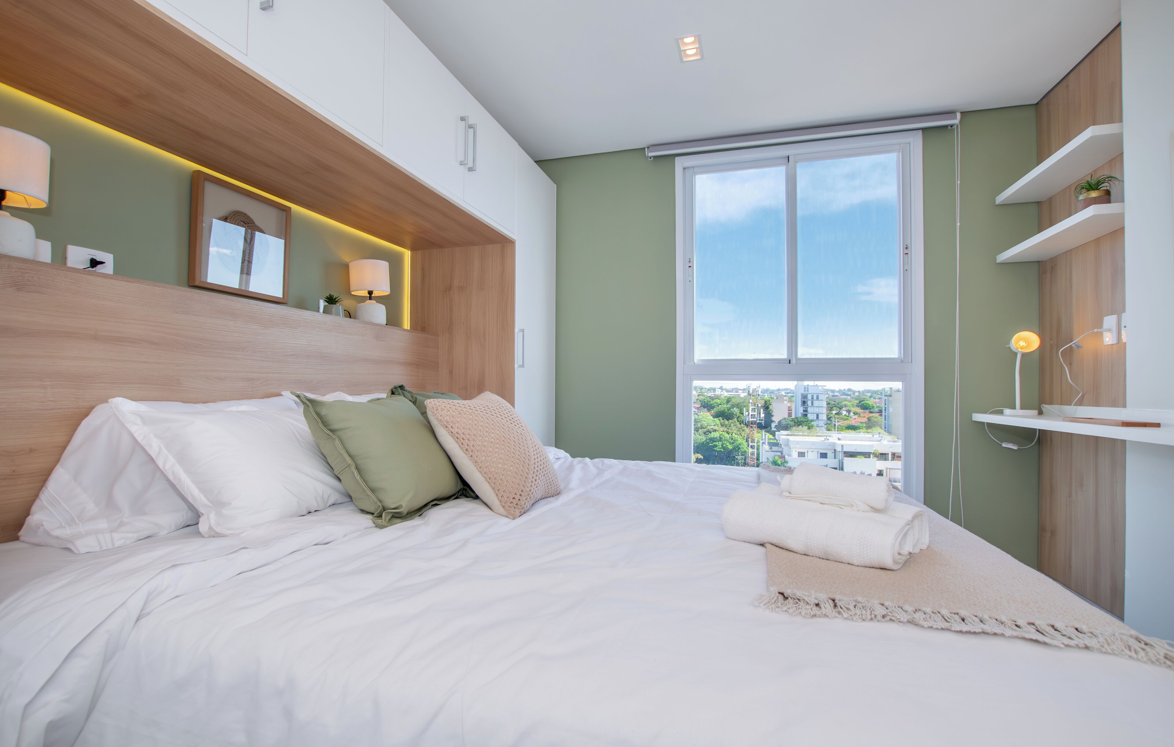 A modern bedroom with a large bed, a view of the city, and a wooden headboard.