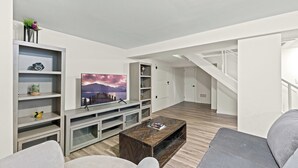 A modern living room with a flat-screen TV, wooden coffee table, and grey sofas.