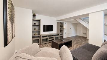 A modern living room with a flat-screen TV, built-in shelving, and a staircase leading to an upper level.