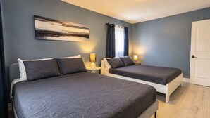 A hotel room with two beds, a painting on the wall, a door, and a window with curtains.