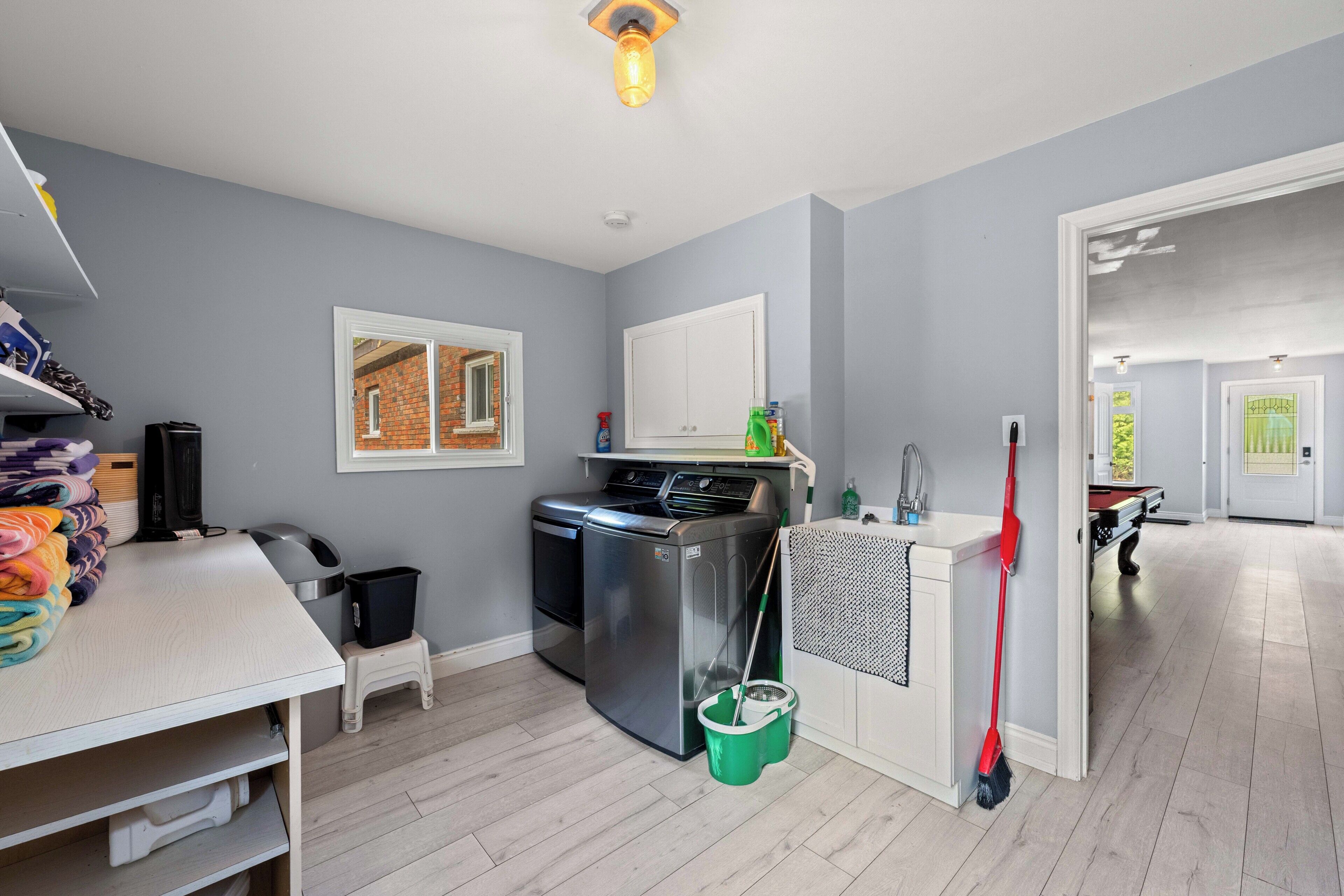 A laundry room with a washing machine, drying rack, and a mop.