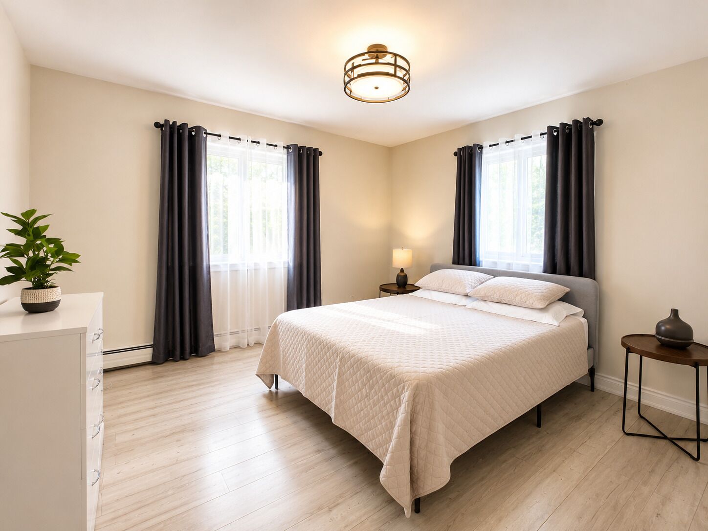 Une chambre à coucher avec un lit, une table de chevet, une lampe, une plante en pot et une fenêtre avec des rideaux.