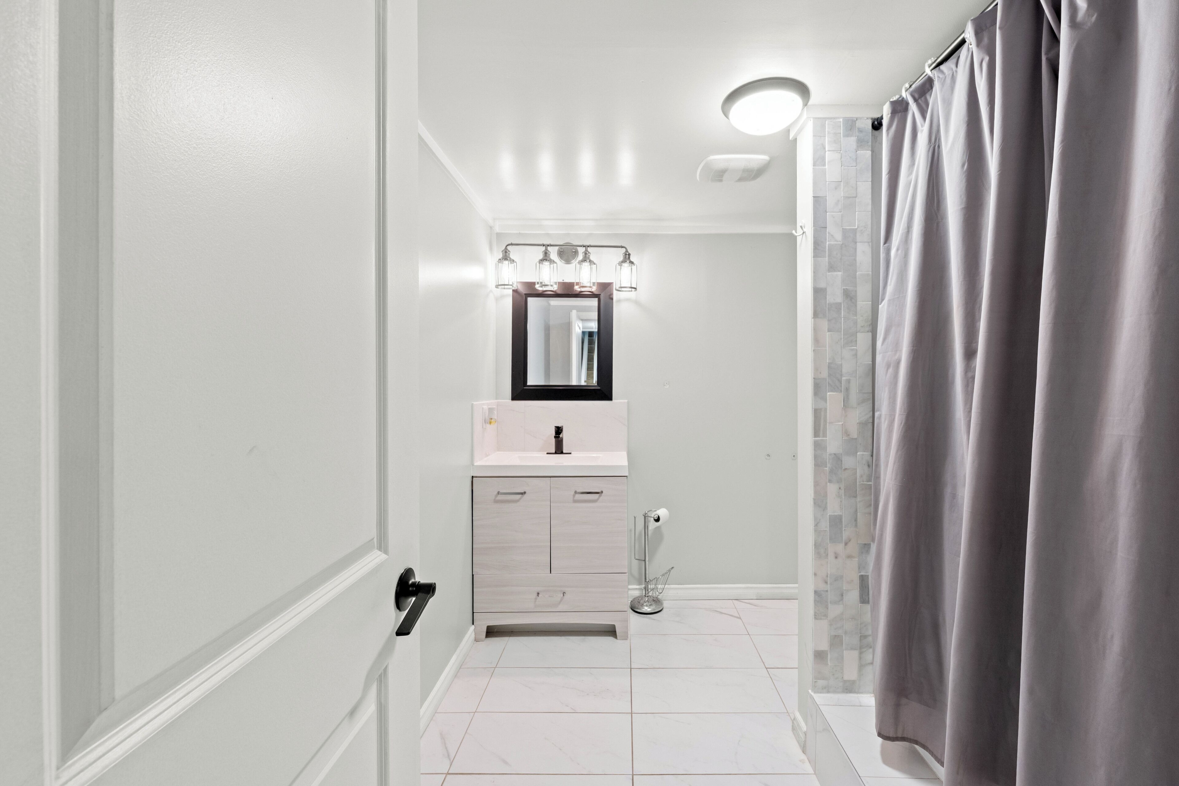 A bathroom with a white vanity, a mirror, a towel rack, and a shower curtain.