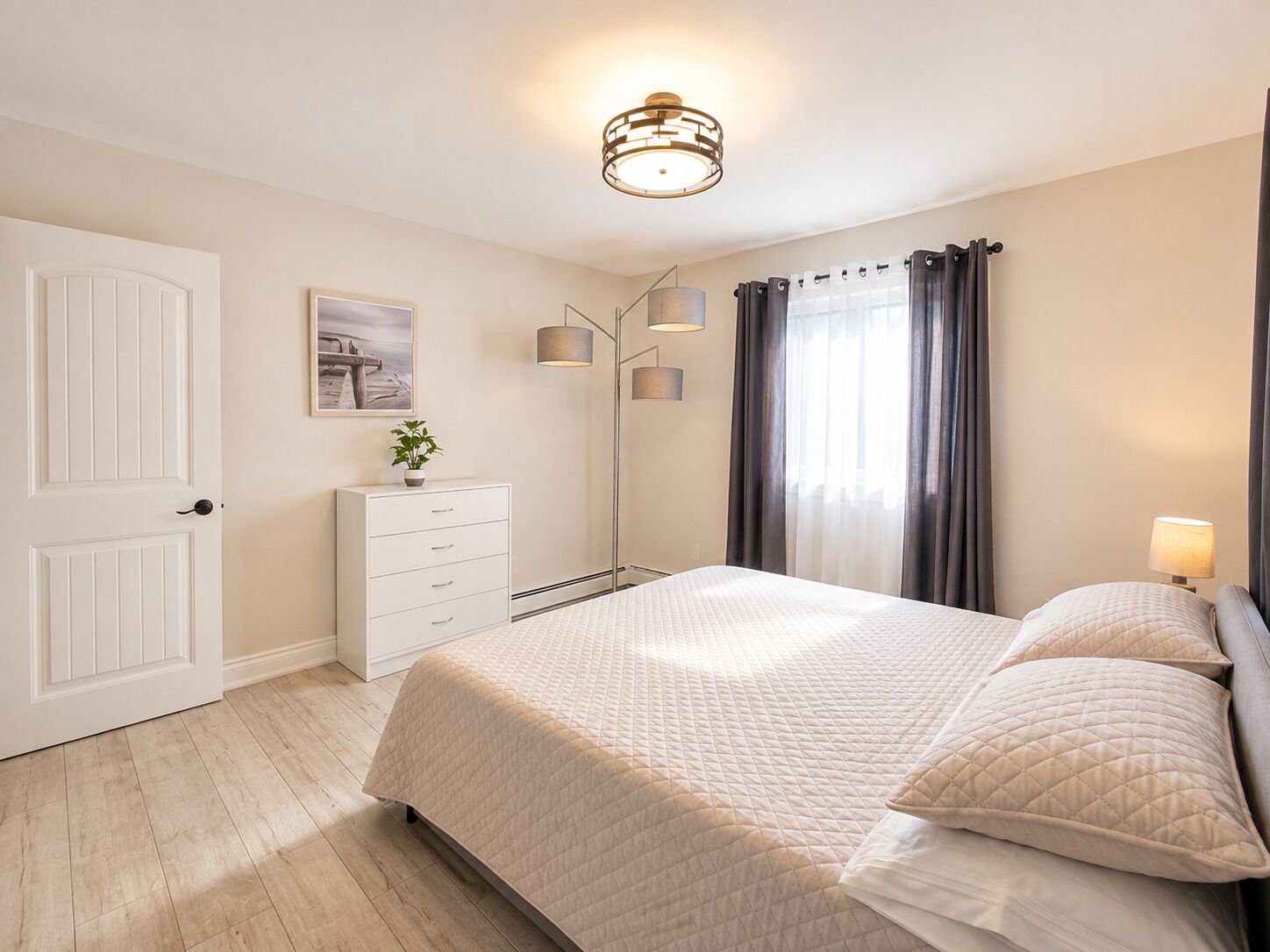 Ein Schlafzimmer mit einem Bett, Nachttischen, einer Stehlampe, einem Gemälde und einer Tür.