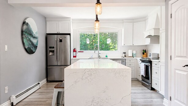 A modern kitchen with a central island, stainless steel appliances, and a large window.