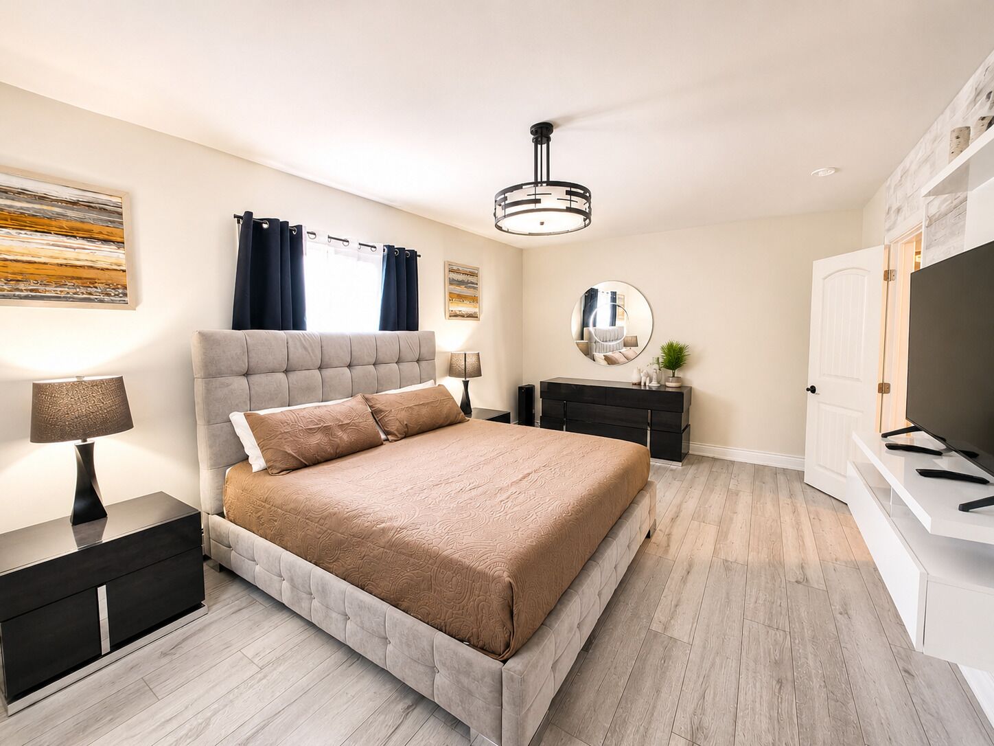Une chambre moderne avec un grand lit, des tables de chevet, un miroir, un ventilateur de plafond et un téléviseur.