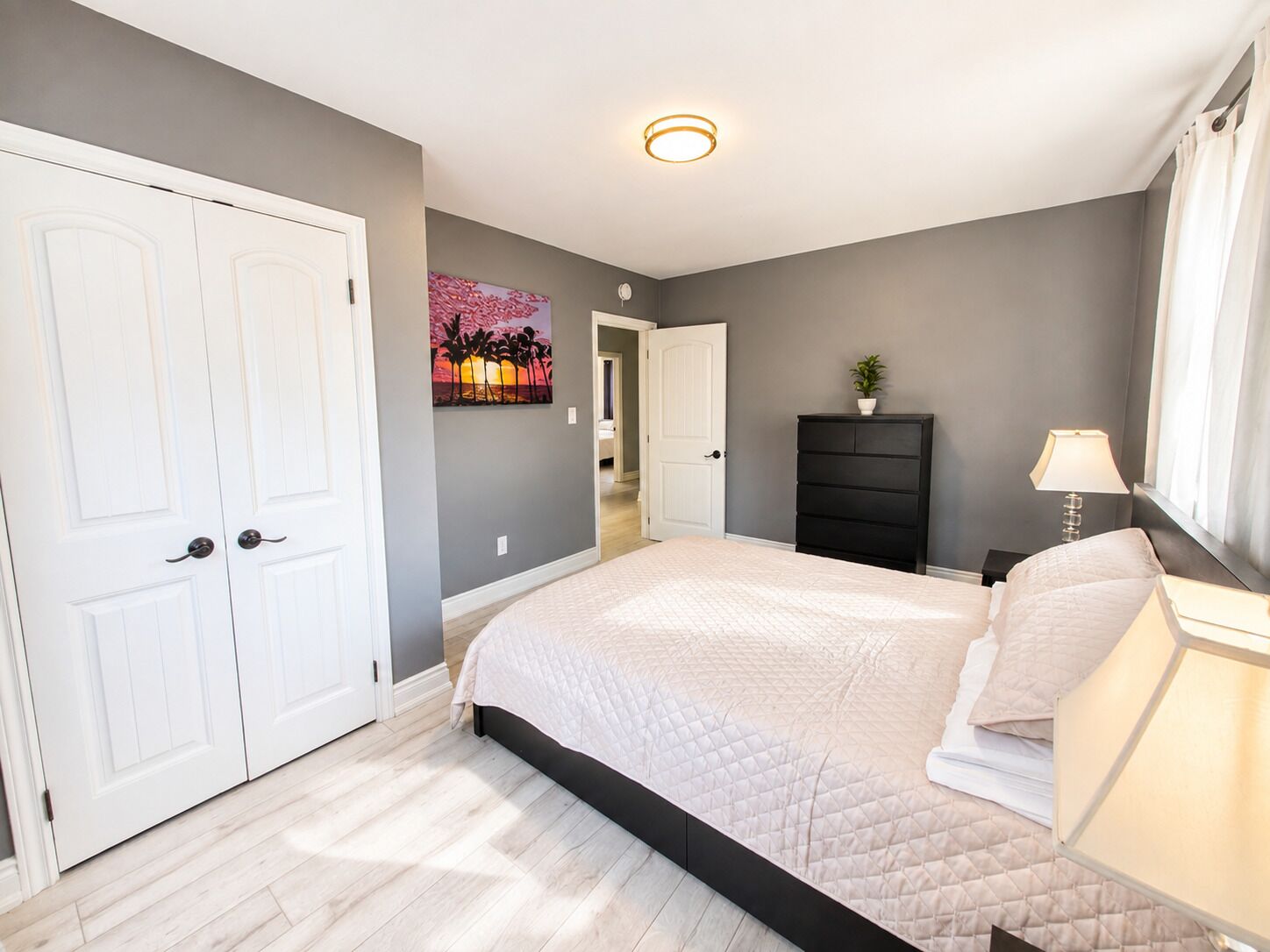 A bedroom with a bed, a dresser, a nightstand, a lamp, and a door.