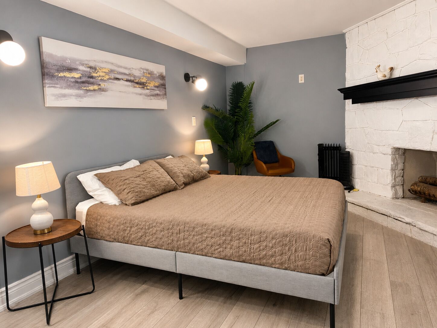 Un dormitorio moderno con cama, lámparas de noche, un cuadro, una planta en maceta y una chimenea.