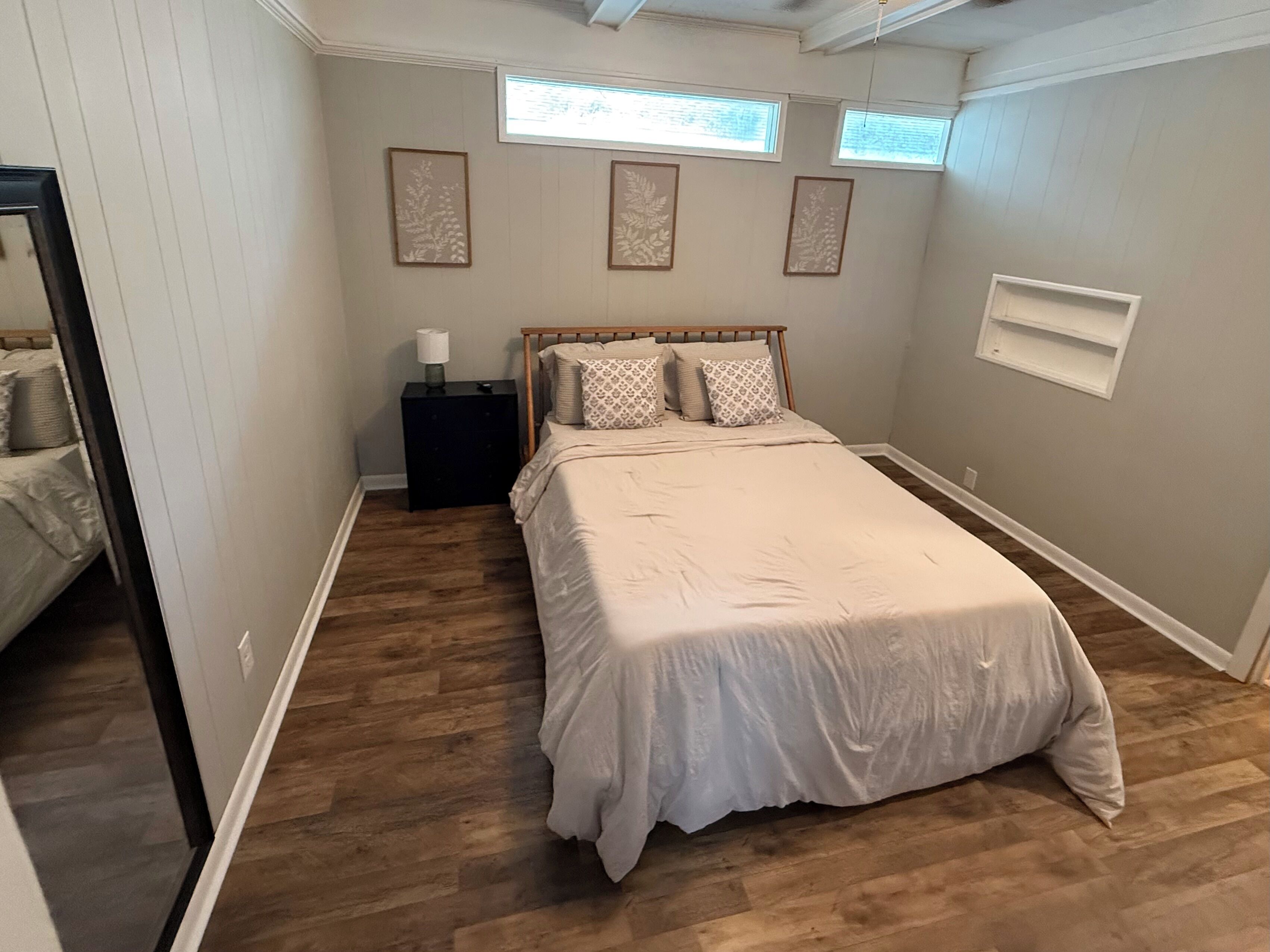 A bedroom with a large bed, a nightstand, a window, and a wall-mounted shelf.
