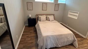 A bedroom with a large bed, a nightstand, a window, and a wall-mounted shelf.