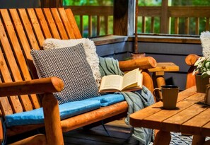 A wooden deck with a wooden chair, a table, and a book. - Rustic Cabin with Fire Pit and Hot Tub (Pigeon Forge)