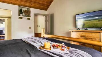 Een slaapkamer met een bed, een houten hoofdbord, een televisie, een plank met decoratieve objecten, en een deur naar een andere kamer.
