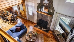 Interior acogedor de una cabaña con comedor, chimenea, sofá y televisor.