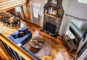 Ein gemütliches Blockhauss-Interieur mit Essbereich, Kamin, einer Couch und einem Fernseher.
