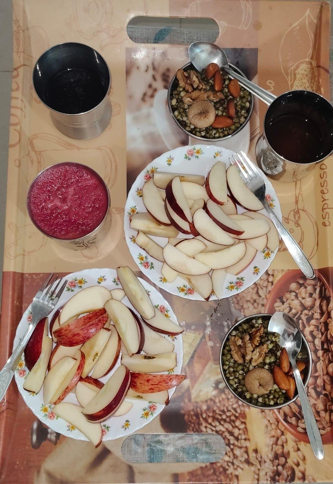 A table with plates of sliced apples, bowls of nuts and seeds, and two cups of a dark liquid, possibly coffee or tea.