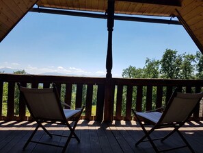 Eine Holzterrasse mit zwei Liegestühlen, die einen schönen Blick auf Berge und Bäume bietet.