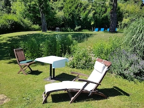 A garden with two wooden chairs and a table, surrounded by lush greenery and trees.