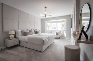 A modern bedroom with a large bed, bedside tables, a dresser, a mirror, and a window with natural light.