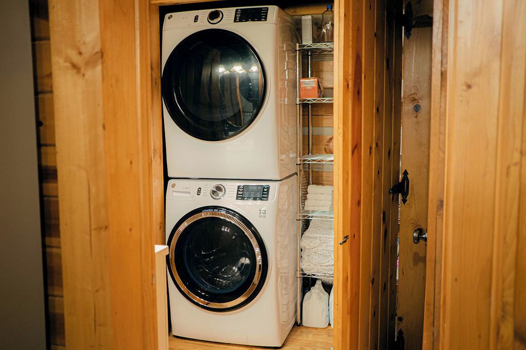 A laundry room with two stacked washing machines and a wooden door.