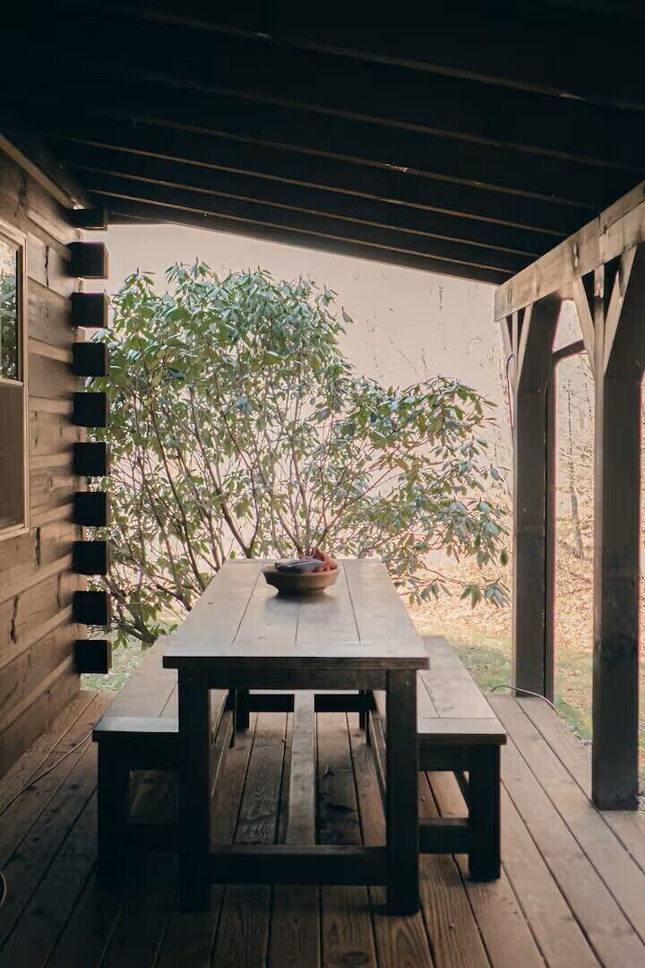 A wooden table with benches in a covered outdoor area with a view of trees.