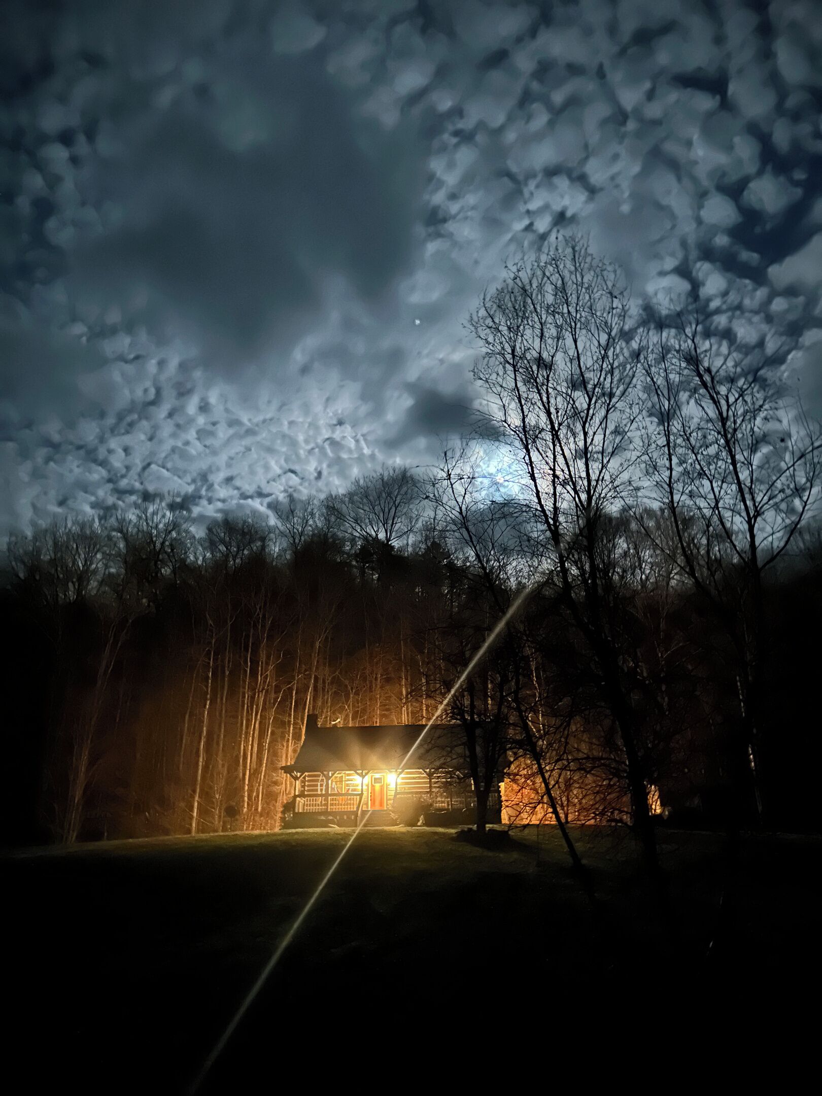 A cabin with a porch, surrounded by trees, under a cloudy sky.