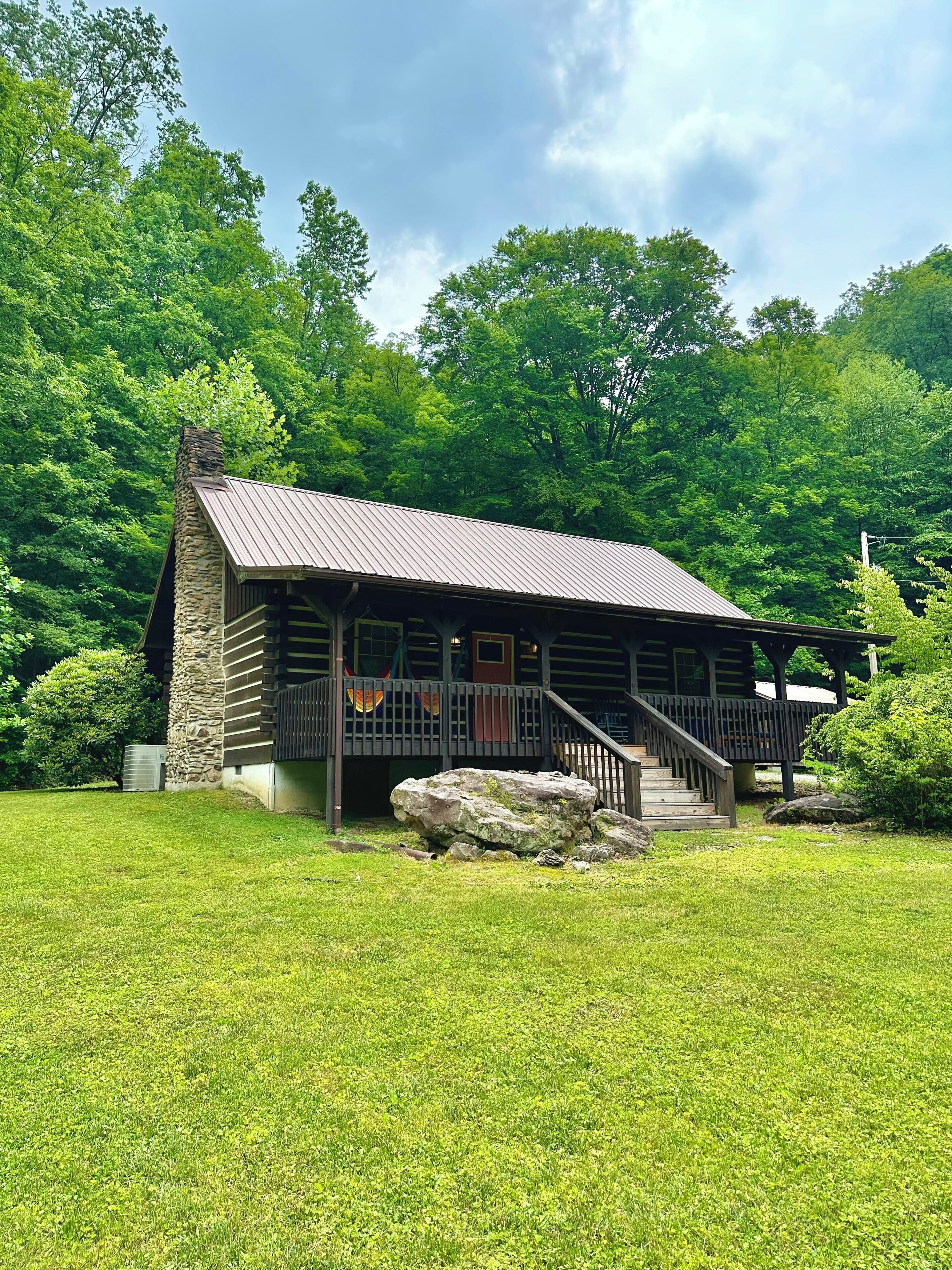 A rustic cabin with a stone chimney, wooden deck, and a staircase leading to a porch.