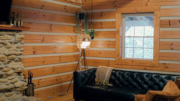 A log cabin interior with a black leather sofa, a round woven coffee table, and a stone wall.