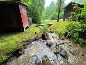 A rustic cabin with a small stream flowing through a grassy area. - The Willow Nest Cabin, Stone fireplace, Cornhole, Kayaks, Views, Porch (Stanton)