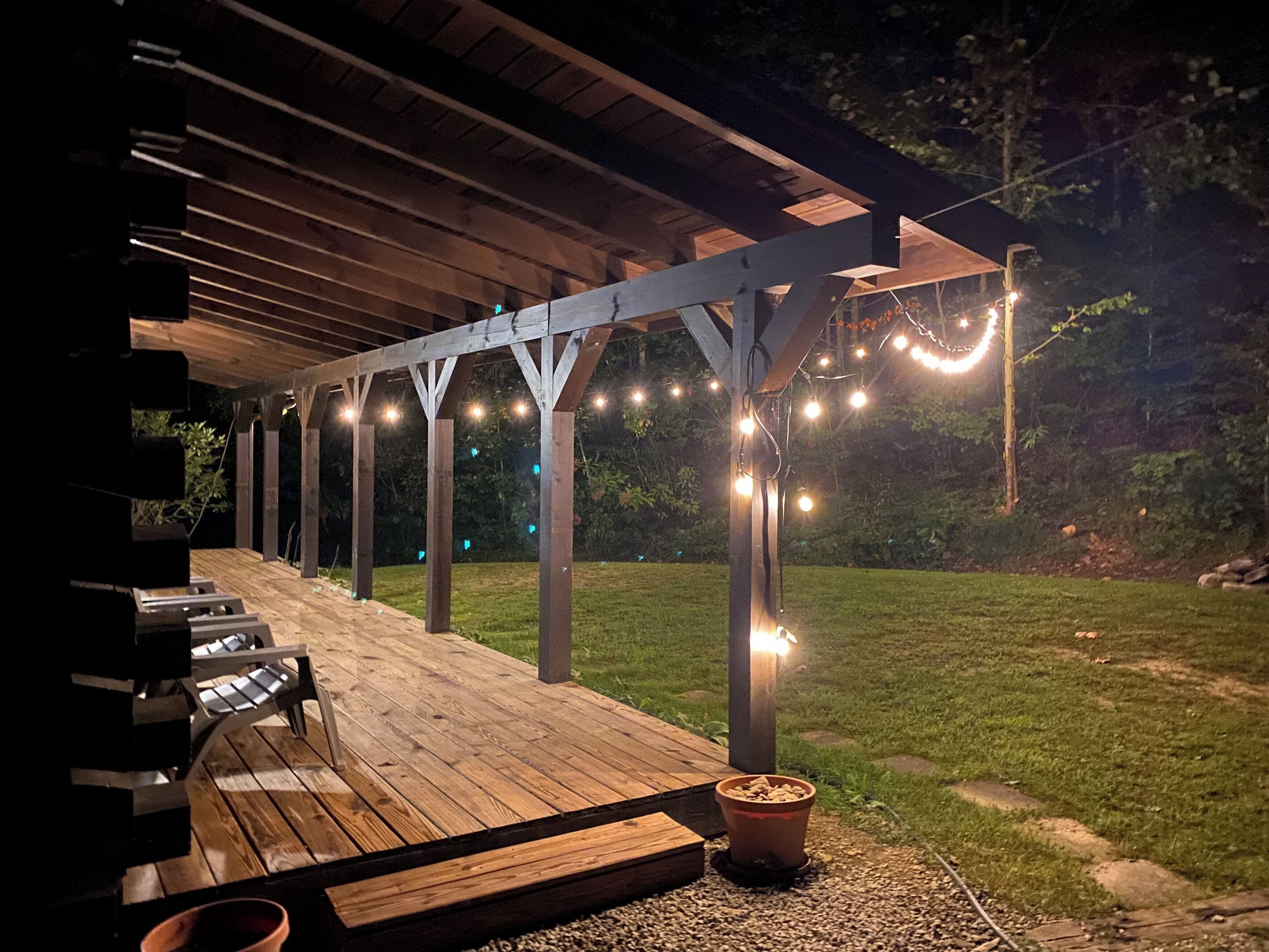 An outdoor covered patio with wooden flooring, a barbecue grill, and string lights.
