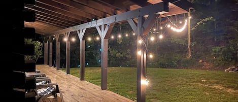 Un patio cubierto al aire libre con piso de madera, una parrilla y luces colgantes.