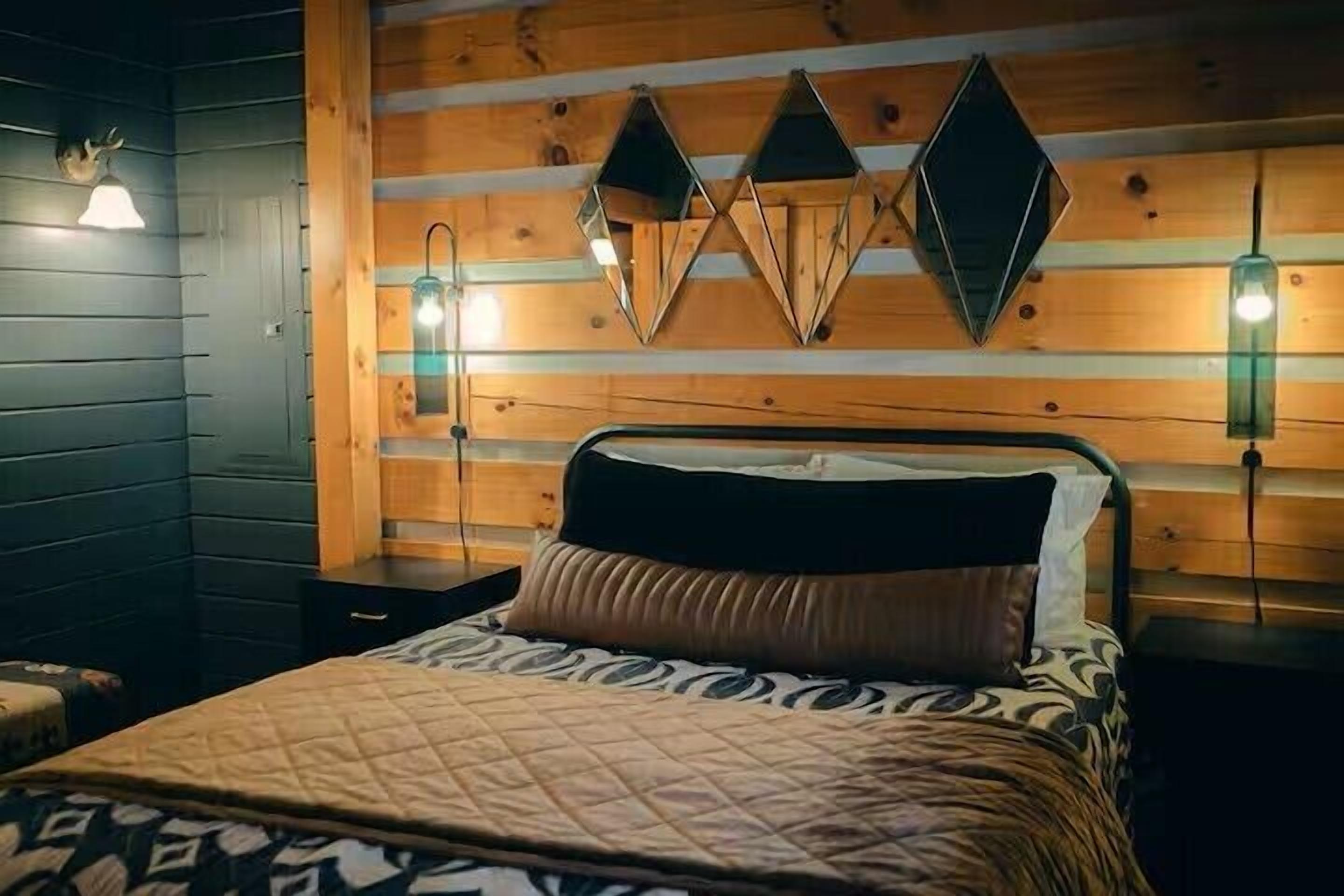 A wooden-paneled room with a bed, two bedside lamps, and a wall-mounted geometric light fixture.