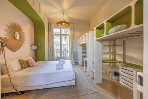 A hotel room with a bed, a desk lamp, a mirror, a window with curtains, and a built-in wardrobe with shelves. - Exceptional Family Apartment 8P A/c- Victor Hugo (Paris)