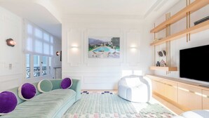 Ein modernes Wohnzimmer mit einem großen Flachbildfernseher, einem Sofa mit violetten Kissen, einem Sitzsack und einem Bild von einem Pool an der Wand.