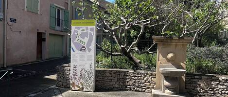 Une cour avec une fontaine en pierre, un panneau indicateur et un bâtiment aux volets verts.