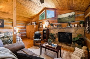 A cozy cabin interior with a fireplace, wooden walls, a comfortable seating area, and a bookshelf. - View  Hot Tub-Sauna-Fire Pit-Fireplace-Honeymoon (Sevierville)