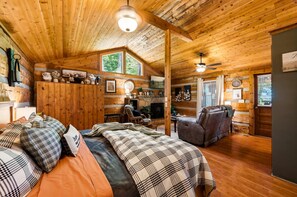 A cozy cabin interior with a bed, a fireplace, a sofa, and a dining area. - View  Hot Tub-Sauna-Fire Pit-Fireplace-Honeymoon (Sevierville)