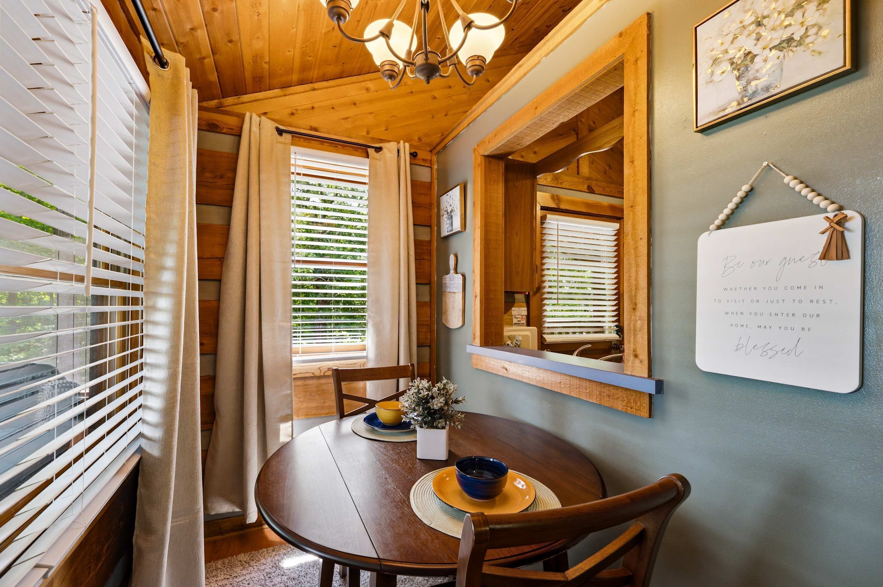 Un intérieur en bois avec une table ronde, des chaises, un lustre et un panneau fixé au mur.