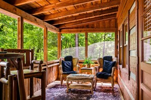 A wooden cabin with wicker furniture, large windows, and a view of a forest. - View  Hot Tub-Sauna-Fire Pit-Fireplace-Honeymoon (Sevierville)