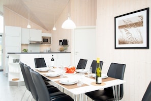A modern kitchen with white cabinets, a microwave, and a dining area with a table set for four. - Serene Wellness Lodge fur 8 Personen (Grossenbrode)
