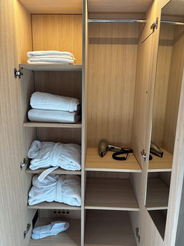 A wooden wardrobe with multiple shelves, some holding folded towels and a pair of slippers.