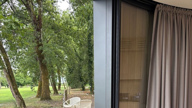 A modern outdoor seating area with a stone pathway leading to a deck, surrounded by trees. - Oomi (Barbaste)