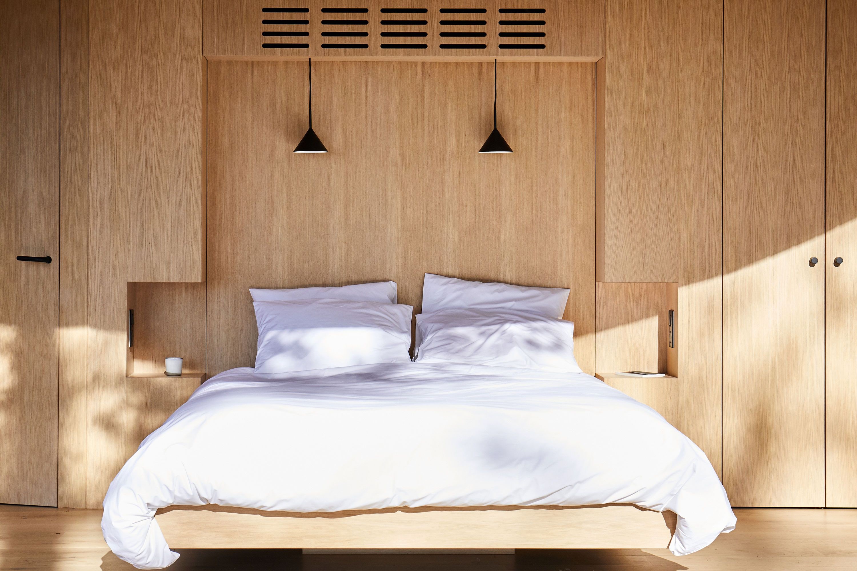 Un dormitorio con estructura de cama de madera, dos mesitas de noche y un armario empotrado.