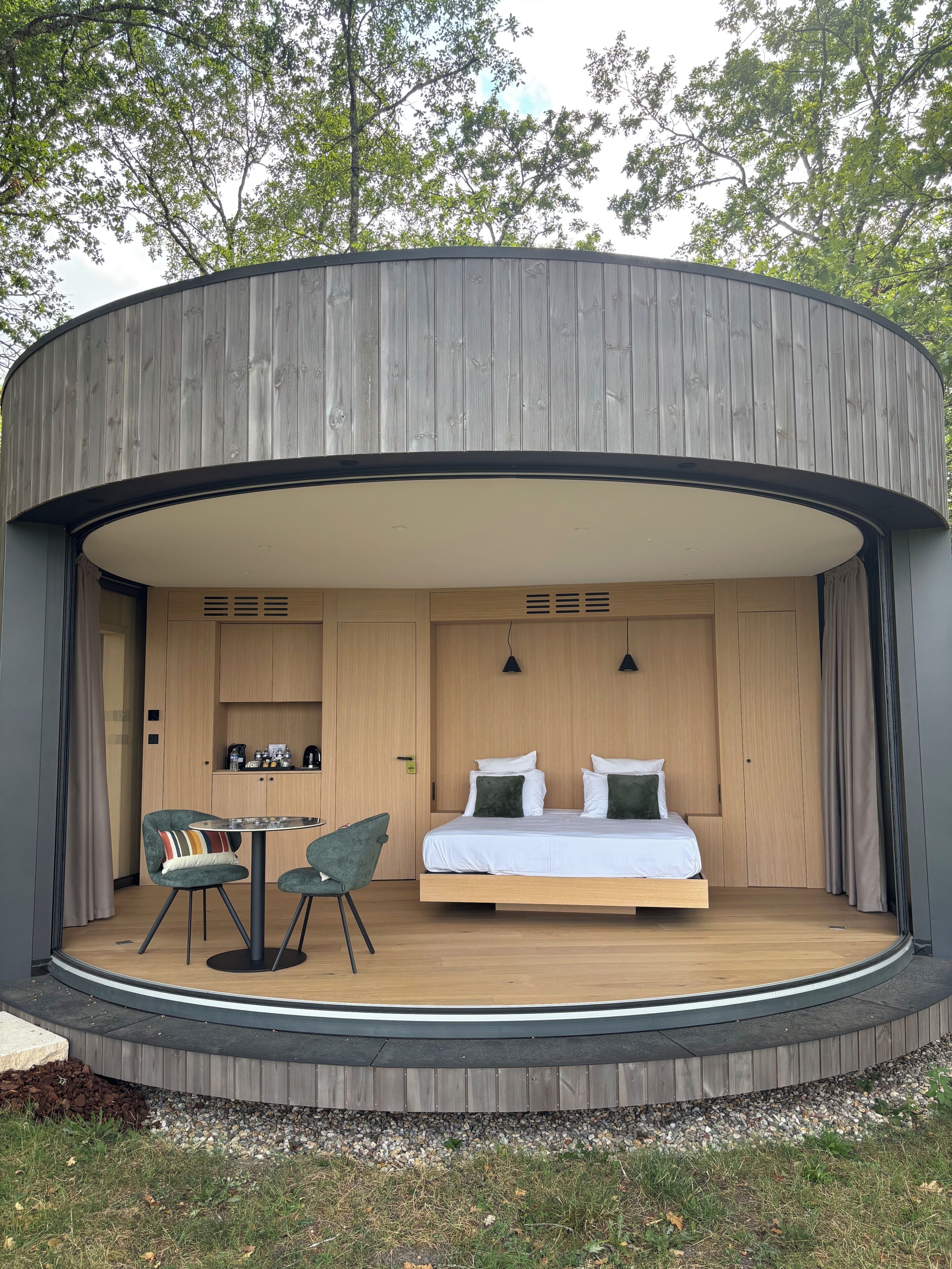 Een ronde houten constructie met een bed, een klein keukentje en een zithoek.