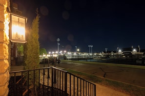 Ein Nachtblick auf einen Parkplatz mit einem Steinhaus, einem kleinen Baum und entfernten Stadionlichtern.