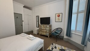 Una camera d'albergo con un letto, una cassettiera, una televisione, una sedia e una finestra con persiane.