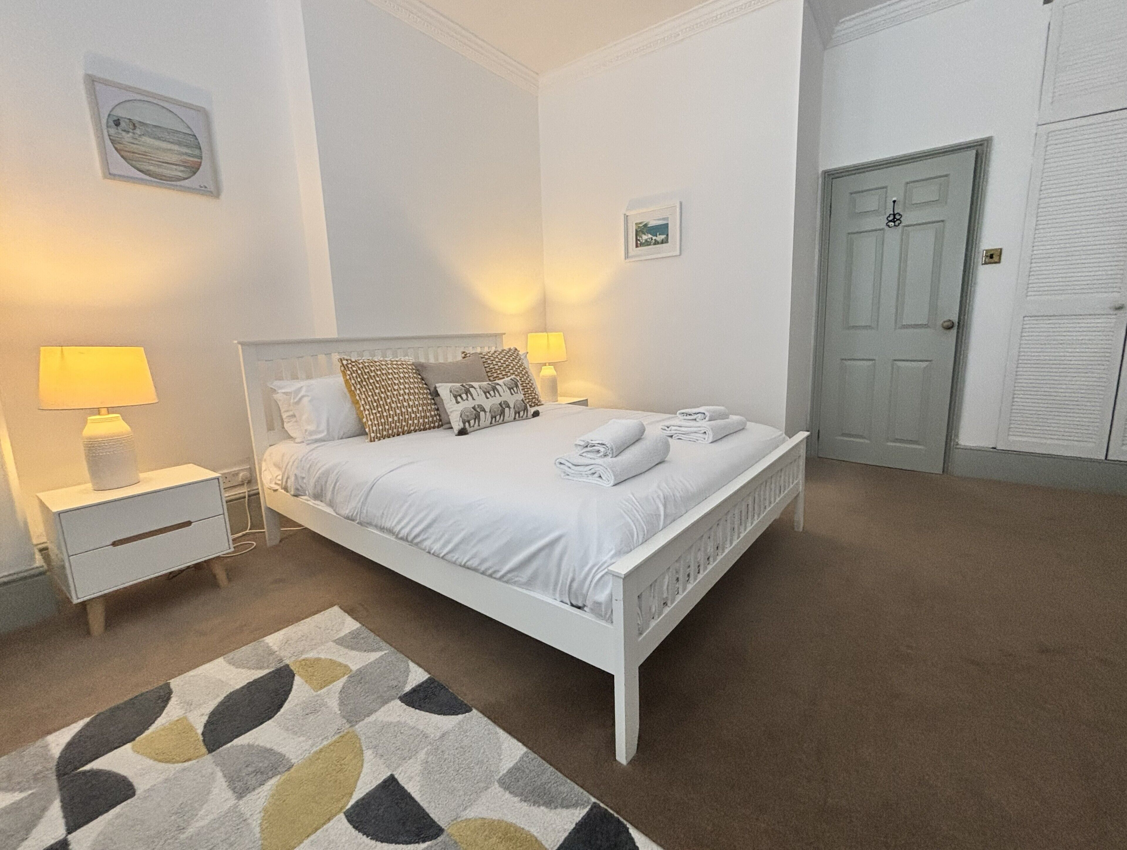 A bedroom with a bed, bedside tables, a nightstand, a lamp, a rug, and a door.