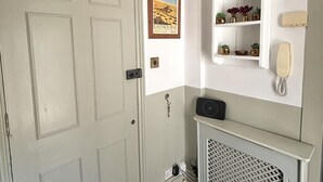 Una stanza con una porta bianca, un quadro appeso al muro, uno scaffale con oggetti decorativi e un termosifone bianco.