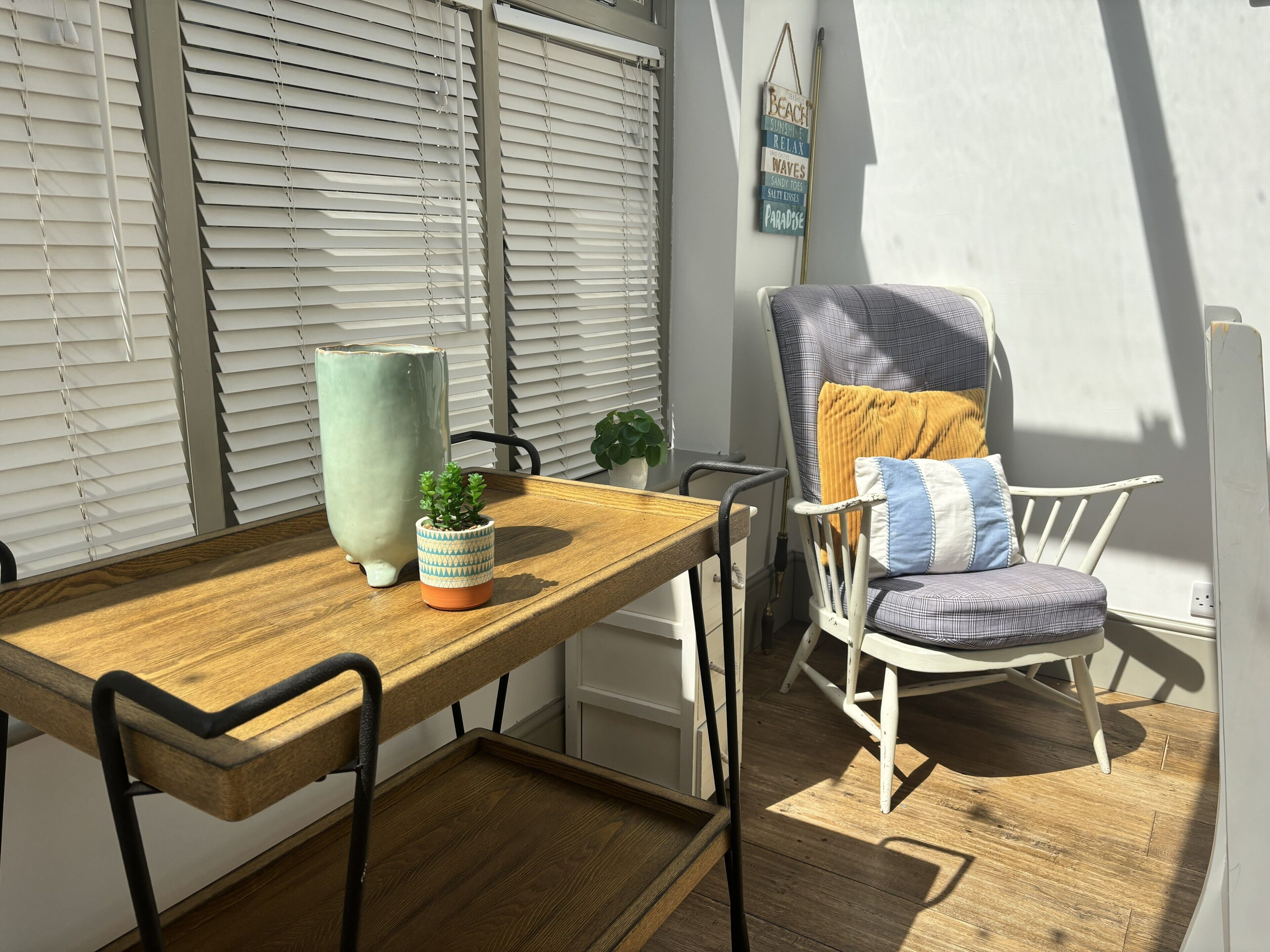 A wooden table with chairs, a potted plant, and a decorative sign on the wall.