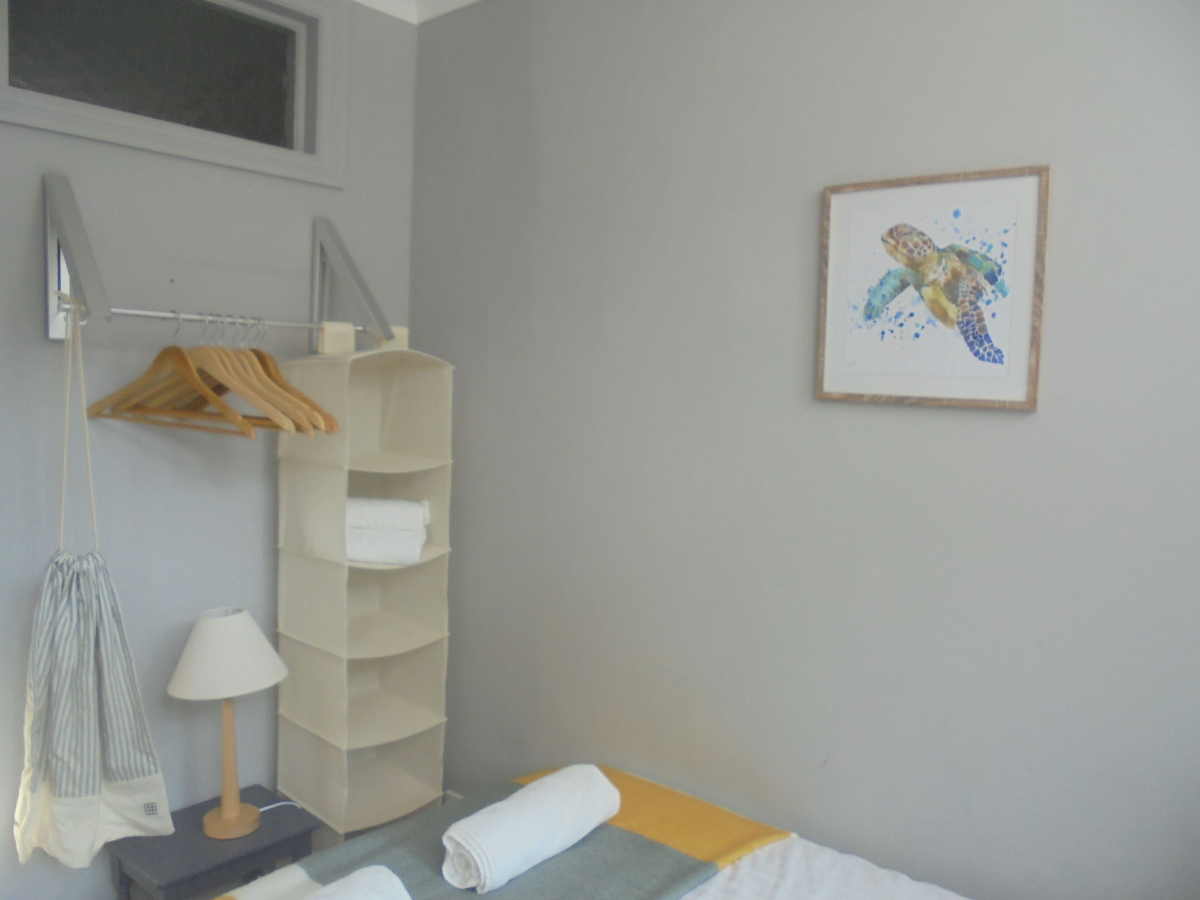 Une chambre d’hôtel avec un lit, une étagère avec des serviettes, un porte-vêtements, une lampe et un tableau encadré au mur.